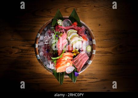 Vue de dessus de savoureux sashimi sain avec des légumes et des herbes servis dans un bol sur une table en bois avec une tranche de saumon frais et radis et citron vert Banque D'Images