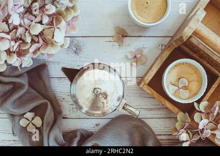 Vue aérienne d'une cafetière vintage en argent, deux tasses de café et hortensias roses Banque D'Images