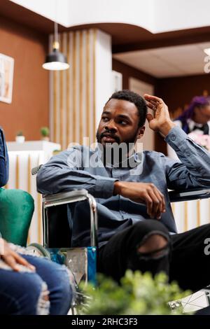 Homme paralysé afro-américain en fauteuil roulant arrivant au centre moderne de rééducation pour personnes handicapées. Touriste handicapé dans le hall de l'hôtel, voyage et vacances pour les personnes handicapées Banque D'Images