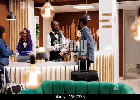 Réceptionniste afro-américaine discutant avec le client, confirmant les détails de la réservation. Le personnel de la réception enregistre les touristes arrivant à la station pendant la saison des vacances, service à la clientèle dans l'hospitalité Banque D'Images