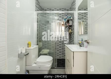 Salle de bains avec meuble-lavabo en bois blanc en porcelaine blanche avec un miroir intégré dans le mur, et une cabine de douche avec cloisons en verre et un Banque D'Images