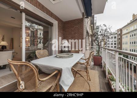 Terrasse d'une maison d'habitation dans un ancien bâtiment avec plancher en planches de bois d'acacia avec table et chaises en rotin, tapis de jute, balustrade en métal blanc et strate Banque D'Images