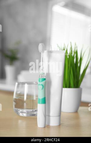 Brosse à dents électrique, tube avec pâte et verre d'eau sur table en bois dans la salle de bain Banque D'Images