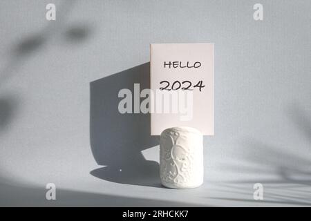 Bonjour 2024 imprimé sur une carte blanche, sur un support blanc avec ombre sur le mur. Banque D'Images