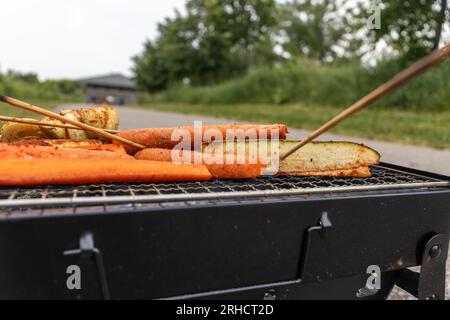 Griller avec des brochettes de légumes - carottes assaisonnées, courgettes et oignons sur un gril rectangulaire noir - fond de chaussée gris Banque D'Images