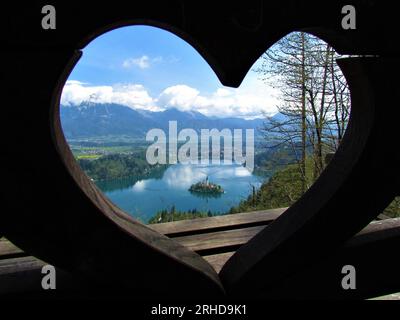 Vue sur le lac de Bled et l'île avec l'église de pèlerinage de l'Assomption de Maria à travers une fenêtre en forme de coeur et des montagnes Banque D'Images