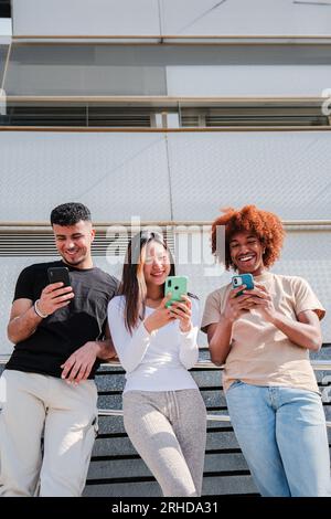 Portrait vertical d'un groupe d'adolescents heureux multiraciaux utilisant un smartphone ensemble pour partager des photos sur un réseau social. Jeunes amis multiethniques s'amusant à naviguer sur Internet en utilisant un téléphone portable. Photo de haute qualité Banque D'Images