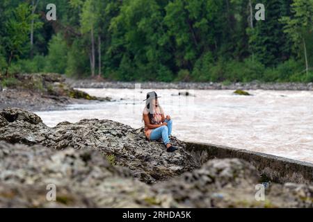 Première nation autochtone canadienne Wet'suwet'en Femme observant les gens pêcher le saumon dans la rivière Bulkley, Witset Canyon, Colombie-Britannique, Canada. Banque D'Images
