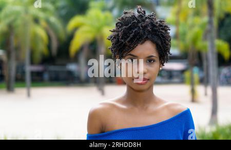 Belle jeune femme adulte afro-américaine avec les cheveux bouclés en plein air avec des paumes Banque D'Images