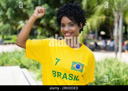 Jeune femme excitée du Brésil avec maillot de football jaune à l'extérieur en été Banque D'Images