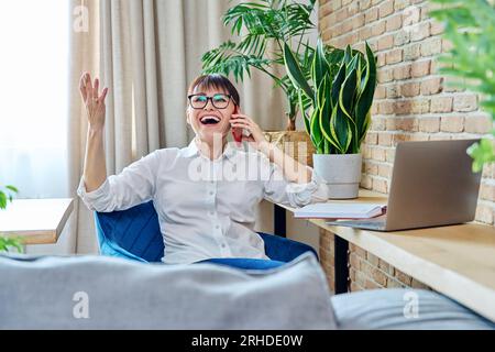 Heureuse femme d'âge moyen parlant sur le téléphone portable, à la maison Banque D'Images