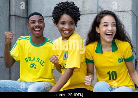 Groupe de fans de football acclamés du Brésil avec le football jaune à l'extérieur en jersey d'été Banque D'Images