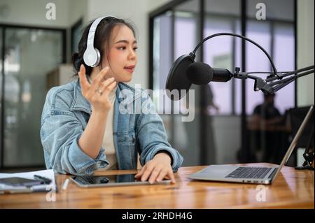 Une animatrice de radio ou podcasteuse asiatique professionnelle parle dans un micro, annonce des nouvelles et diffuse son podcast audio en direct dans le stud Banque D'Images