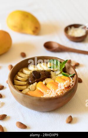 Grand angle de bol en bois rempli de noix appétissantes et de fruits frais garnis de feuilles de menthe placées sur une nappe blanche Banque D'Images