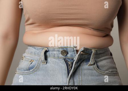 Femme en surpoids en jeans serrés sur fond gris, gros plan Banque D'Images