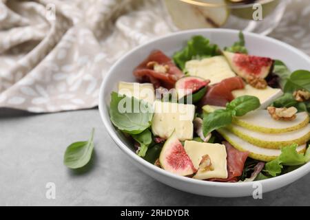 Salade savoureuse avec brie, prosciutto, poire et figues sur table grise, gros plan. Espace pour le texte Banque D'Images