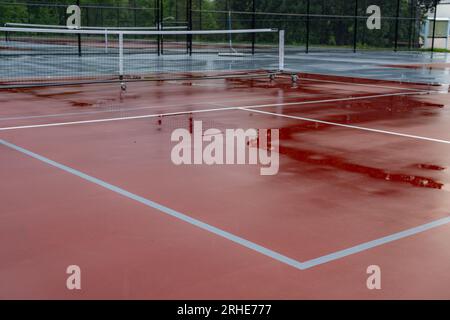 Nouveaux filets de pickleball portables sur un court de tennis rouge humide avec des lignes blanches combinées avec des lignes de pickleball grises Banque D'Images