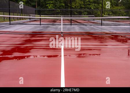 Nouveaux filets de pickleball portables sur un court de tennis rouge humide avec des lignes blanches combinées avec des lignes de pickleball grises Banque D'Images