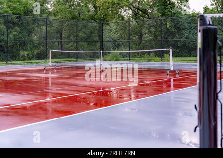 Nouveaux filets de pickleball portables sur un court de tennis rouge humide avec des lignes blanches combinées avec des lignes de pickleball grises Banque D'Images