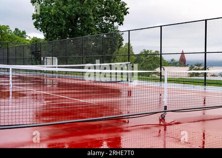 Nouveaux filets de pickleball portables sur un court de tennis rouge humide avec des lignes blanches combinées avec des lignes de pickleball grises Banque D'Images