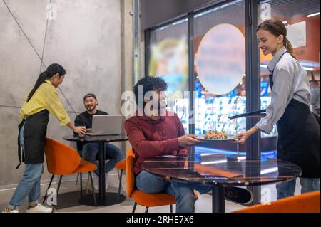 Serveuse souriante passant l'assiette avec des sushis au client au café Banque D'Images