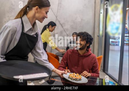 Serveuse souriante passant l'assiette avec des sushis au client au café Banque D'Images