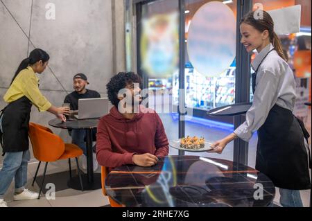 Serveuse souriante passant l'assiette avec des sushis au client au café Banque D'Images