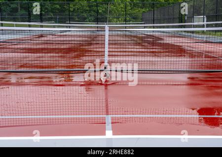 Nouveaux filets de pickleball portables sur un court de tennis rouge humide avec des lignes blanches combinées avec des lignes de pickleball grises Banque D'Images