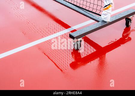 Nouveaux filets de pickleball portables sur un court de tennis rouge humide avec des lignes blanches combinées avec des lignes de pickleball grises Banque D'Images