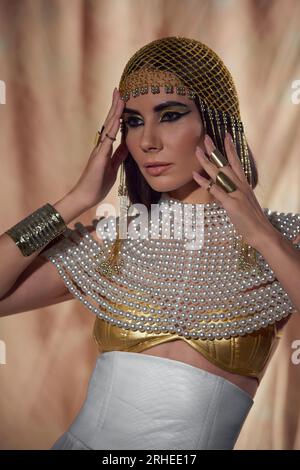 Portrait de femme brune en costume égyptien et collier de perles debout sur fond abstrait Banque D'Images