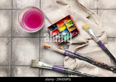 Peintures d'artiste avec des pinceaux, tissu et verre sur fond de carreaux gris Banque D'Images