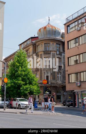 Les gens marchent le long d'une rue dans la nouvelle partie de Sarajevo un jour d'été avec un bâtiment d'angle en dôme pittoresque , Bosnie-Herzégovine, 16 août 2023. Banque D'Images