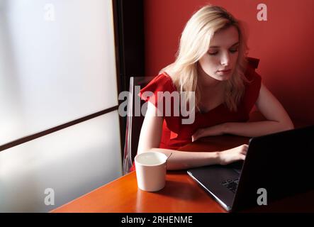 Jeune femme adulte portant une combinaison rouge et utilisant un ordinateur portable Banque D'Images