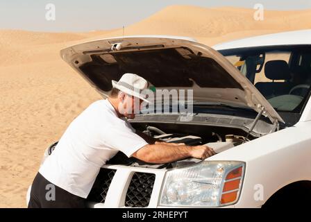Un homme inspecte le moteur de son véhicule hors route dans la chaleur brûlante du désert aride du Moyen-Orient. Banque D'Images