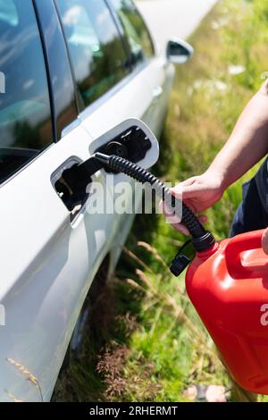 Le conducteur remplit le réservoir vide de la voiture à partir d'une cartouche rouge sur le côté de la route. Gros plan, photo verticale Banque D'Images