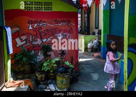 Bandung, Indonésie. 16 août 2023. Un enfant marche à travers un mur avec de la peinture colorée et des décorations dans les tons de rouge et de blanc qui ornent une ruelle à Cikudapateh Dalam, Bandung, Java Ouest, Indonésie le mardi 16 2023 janvier. Les ornements et décorations des résidents de cette colonie densément peuplée s’inscrivent dans le cadre du 78e anniversaire de l’indépendance de la République d’Indonésie le 17 août. (Photo Dimas Rachmatsyah/INA photo Agency/Sipa USA) crédit : SIPA USA/Alamy Live News Banque D'Images