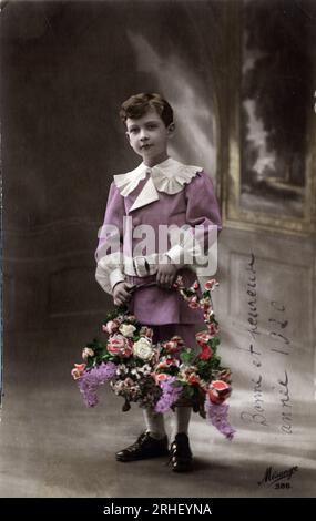 Carte de voeux de bonne annee : un enfant tenant une corde de fleurs - carte postale datee 1920 Banque D'Images