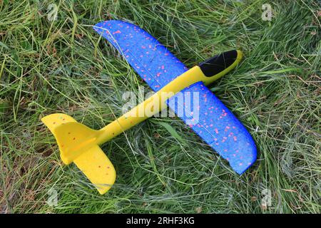 Avion mousse jaune et bleu sur l'herbe dans le parc. Jouets pour enfants Banque D'Images