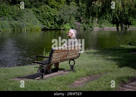 Homme senior assis sur un banc de parc près de la rivière, seul dehors et réfléchi. Angleterre Royaume-Uni Banque D'Images