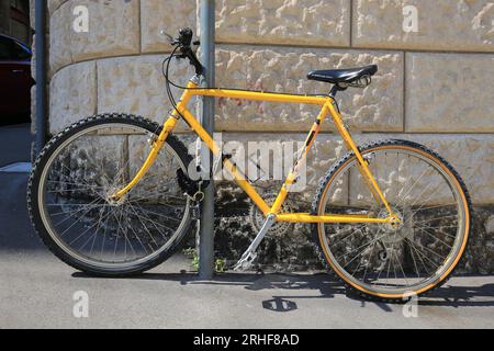 Vélo jaune attaché à un poteau près du mur Banque D'Images