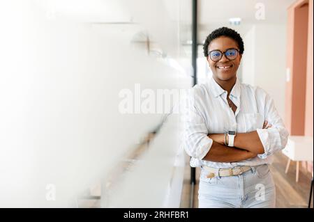 Femme entrepreneure déterminée et fière debout avec les bras croisés dans le couloir du bureau, femme freelance moderne et élégante avec une coupe de cheveux courte regardant la caméra dans l'espace de coworking Banque D'Images