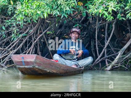 Un homme fumant et pêchant à partir d'un petit bateau sur une rivière. Sumatra, Indonésie. Banque D'Images