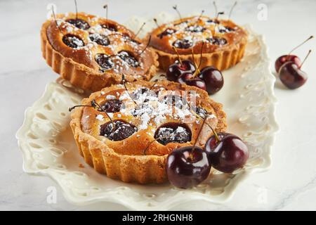 French Flair, Cherry Clafoutis présenté sur White Marble. Tentation alléchante : clafoutis et cerises sur marbre. Banque D'Images