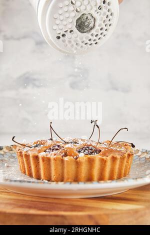 French Flair, clafoutis aux cerises présenté sur marbre blanc saupoudré de sucre en poudre. Banque D'Images