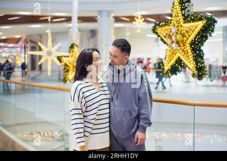 Jeune couple kazakh asiatique, homme et femme se regardent avec amour dans le centre commercial de Noël. jeunes mariés, jeune famille. portrait Banque D'Images