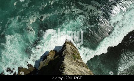 Un rocher pointu d'une vue d'oiseau, ci-dessous est un océan puissant, ses vagues se brisent contre le rocher. Océan bleu intense, avec d'énormes vagues. Banque D'Images