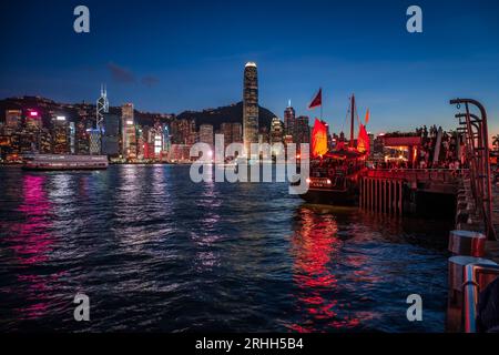 Superbe vue nocturne d'une jonque illuminée dans le port Victoria en face de l'horizon fantastique de Hong Kong avec ses impressionnants gratte-ciel Banque D'Images