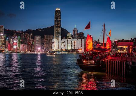 Superbe vue nocturne d'une jonque illuminée dans le port Victoria en face de l'horizon fantastique de Hong Kong avec ses impressionnants gratte-ciel Banque D'Images
