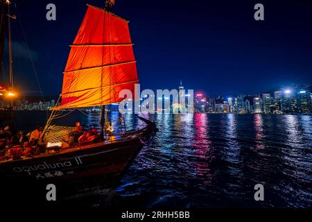 Superbe vue nocturne d'une jonque illuminée dans le port Victoria en face de l'horizon fantastique de Hong Kong avec ses impressionnants gratte-ciel Banque D'Images