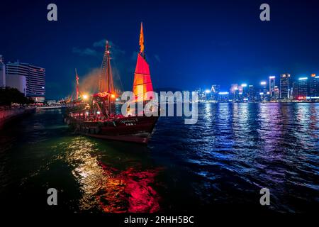 Superbe vue nocturne d'une jonque illuminée dans le port Victoria en face de l'horizon fantastique de Hong Kong avec ses impressionnants gratte-ciel Banque D'Images